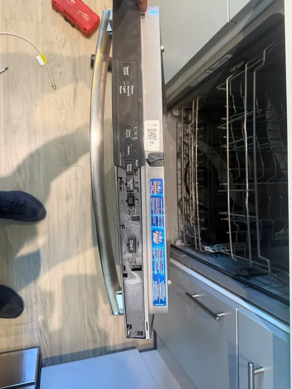 Dishwasher with the door open, showing the control buttons on the top edge of the door and the racks inside