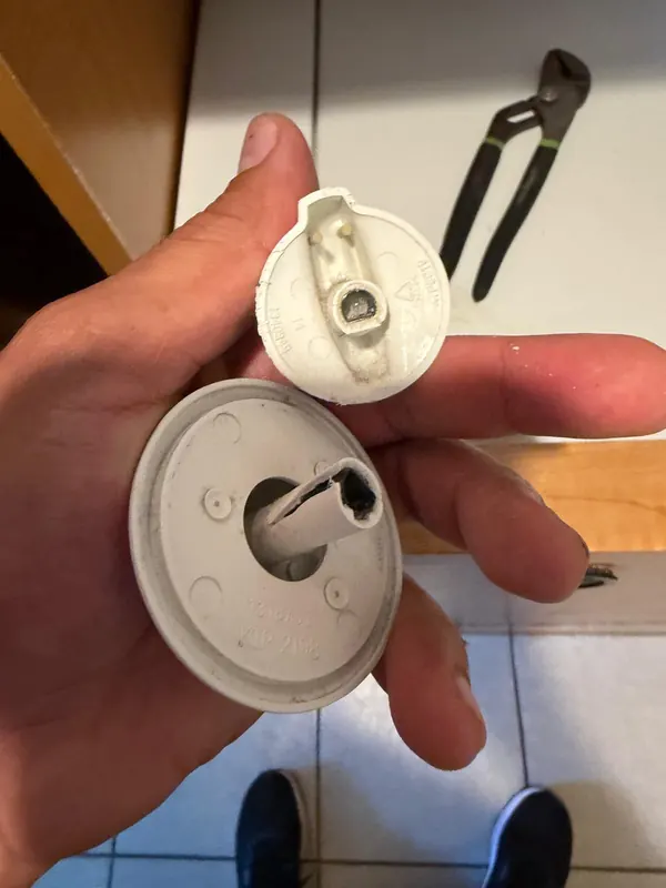 Hand holding two appliance control knobs, one with a cracked plastic shaft insert