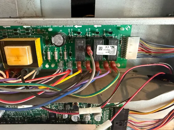 Refrigerator control board with relays, a transformer and wire connectors, exposed behind an access panel