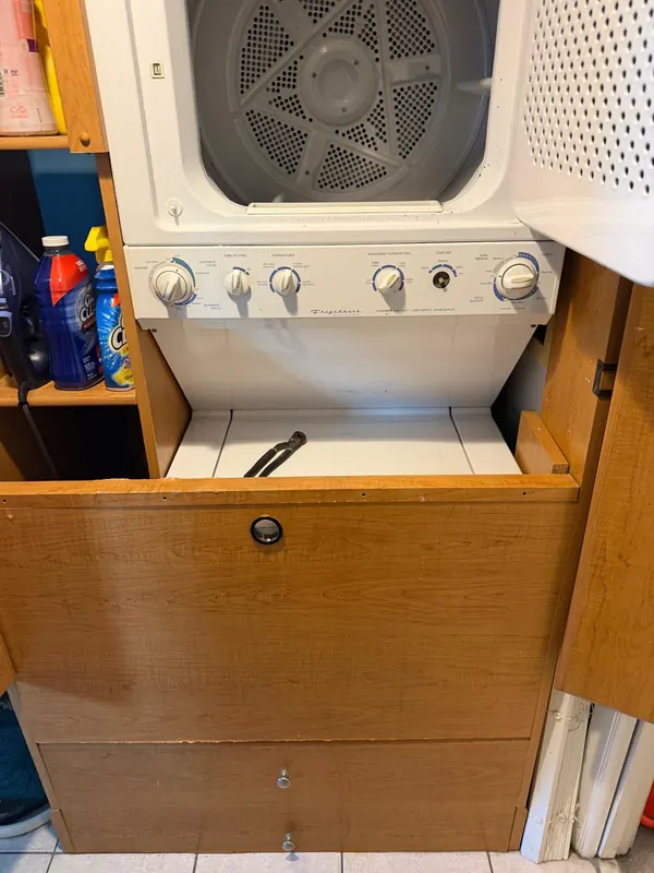 Stacked washer and dryer unit inside a wooden laundry cabinet, with the dryer door open