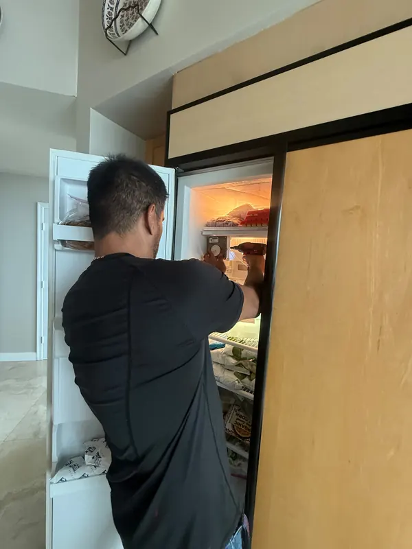 Technician reaching into the open freezer section of a built-in refrigerator with wood panel doors